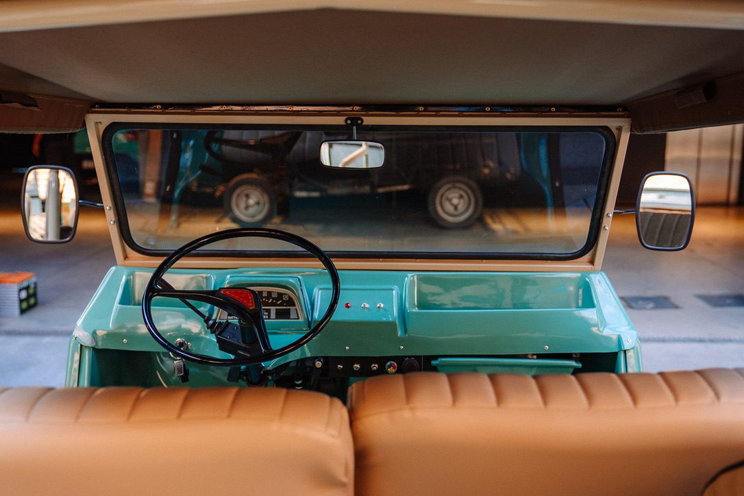 Driver's view of a Méhari — black steering wheel, period dashboard, turquoise body, tan rear seats